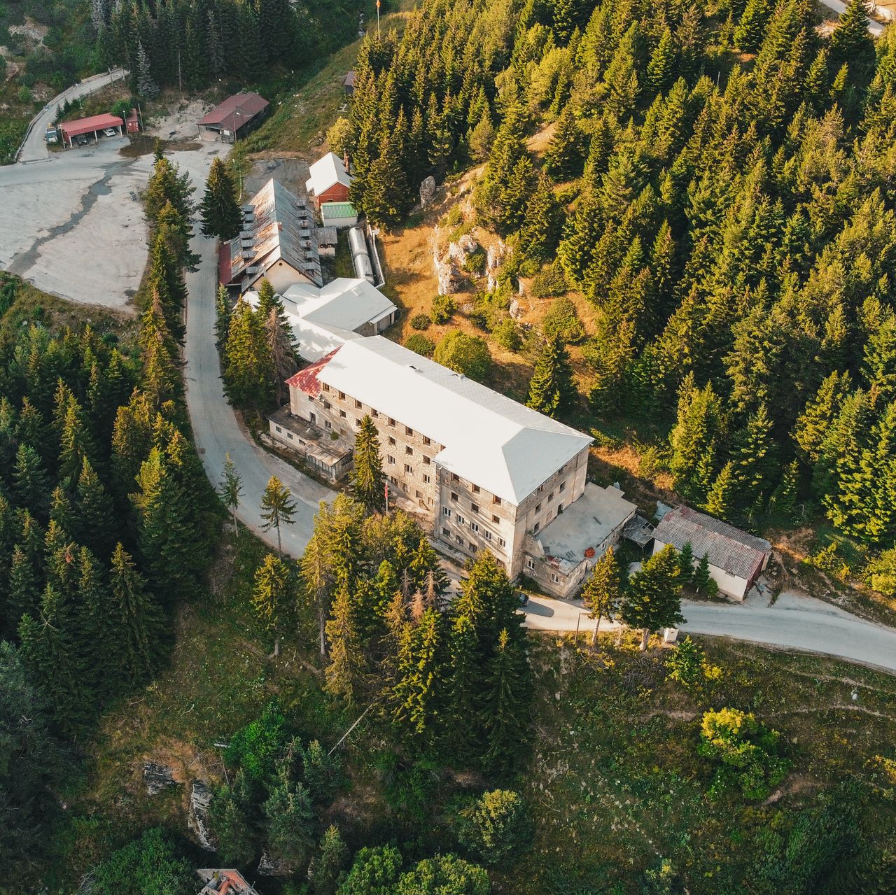 Drone shot of a resort building nestled in lush mountain scenery with winding roads and evergreen trees.
